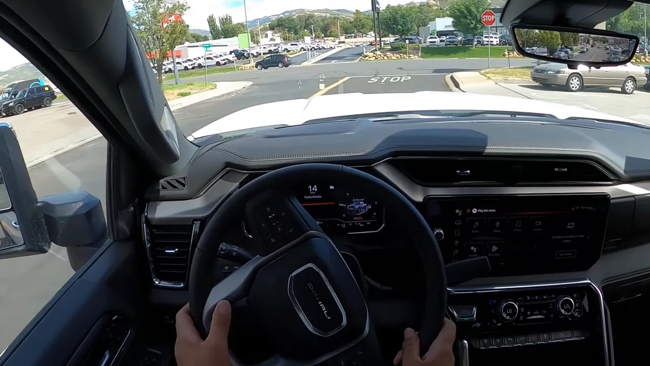 Driver hands on steering wheel with clear hood view, head-up display and STOP marking on the street in a GMC Sierra 3500 Denali