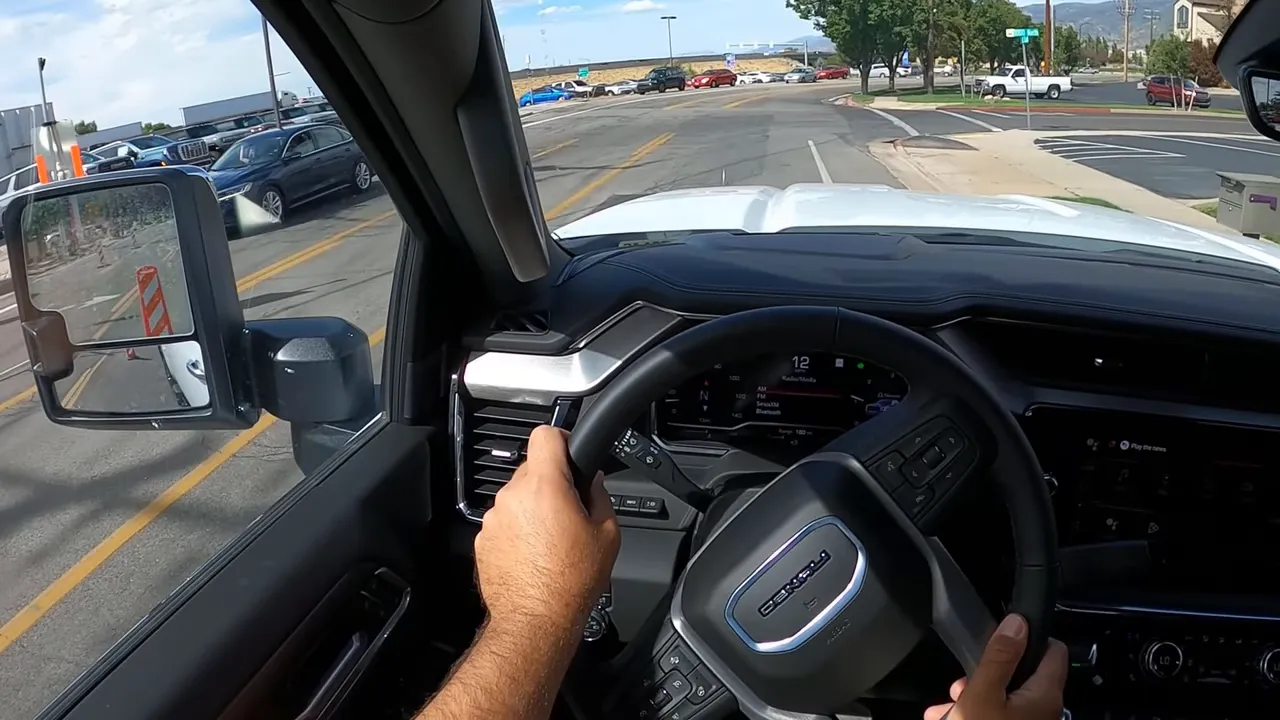 Driver point-of-view with hands on the wheel, visible instrument cluster and road ahead inside a GMC Sierra 3500 Denali