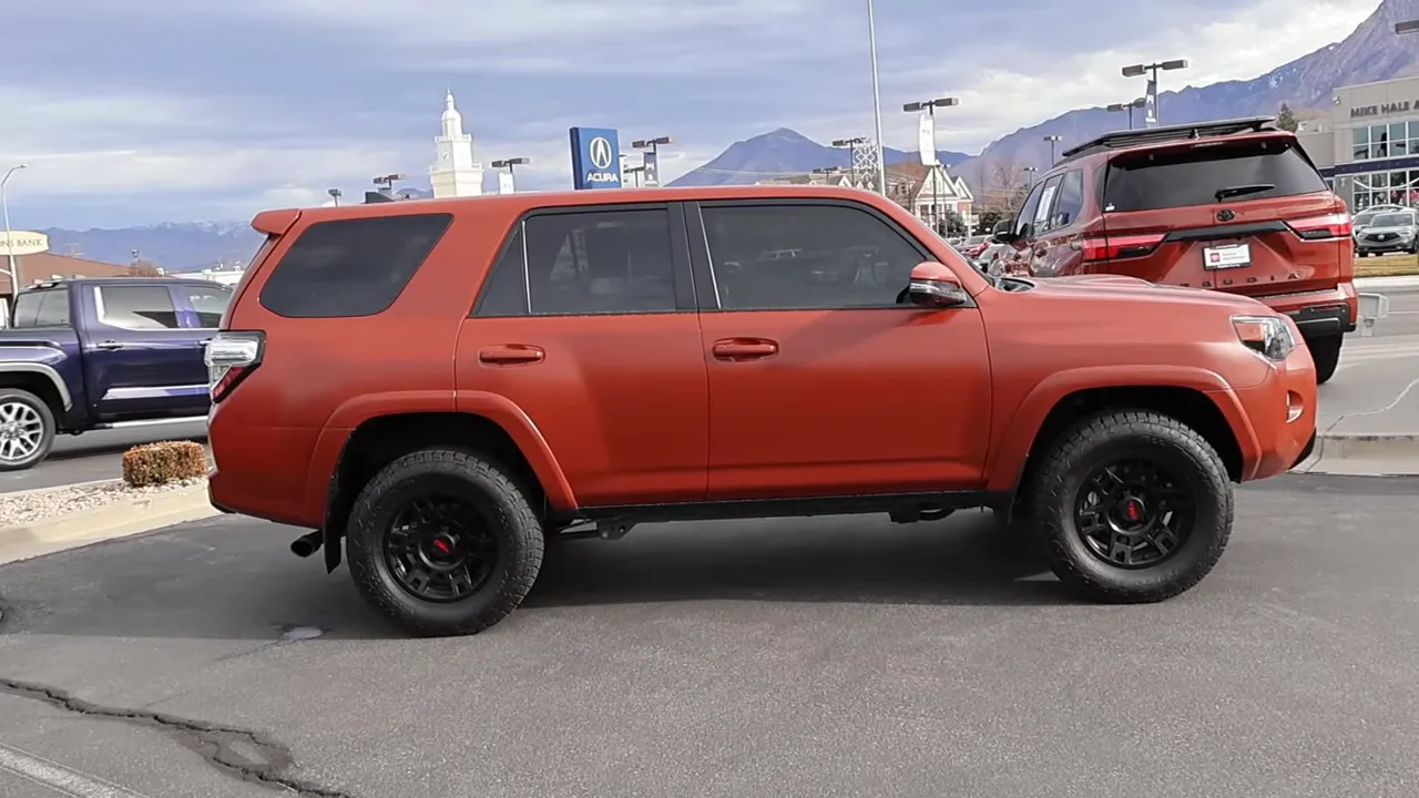 Full side profile of an orange 5th-generation Toyota 4Runner at a dealership, showing wheels and body condition