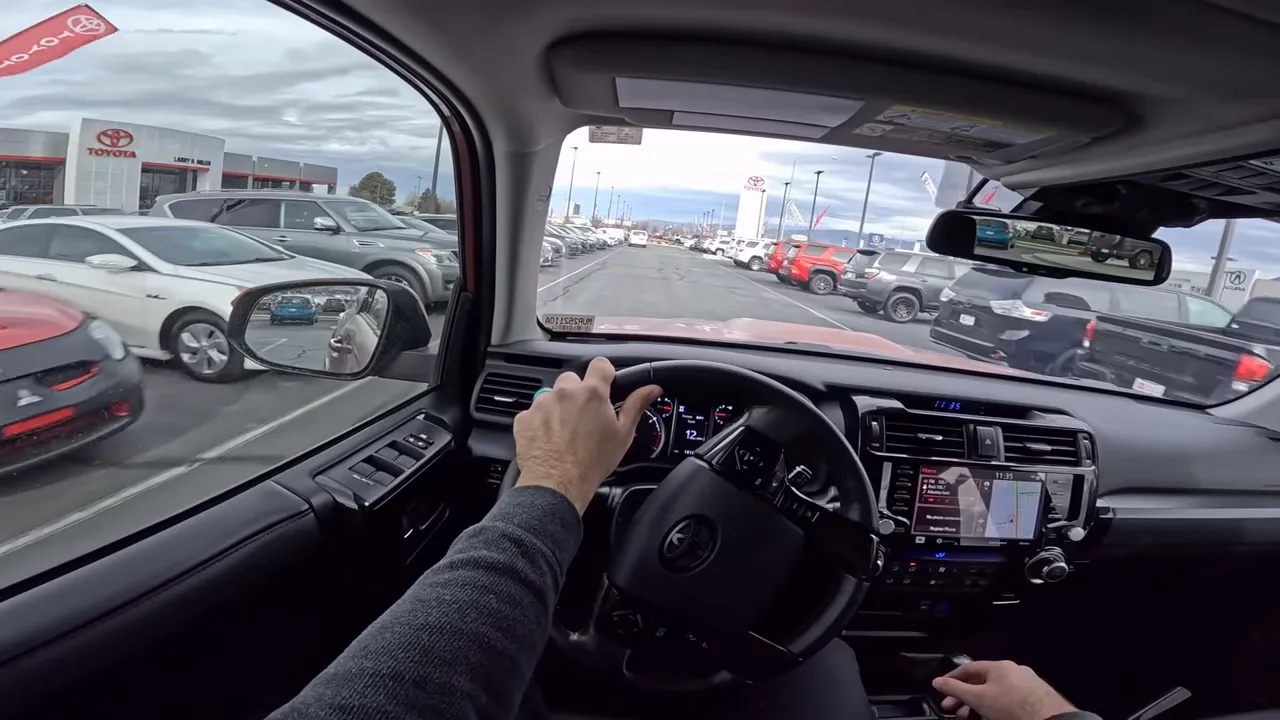 View down a Toyota dealership aisle from inside a 4Runner showing multiple vehicles and Toyota signage