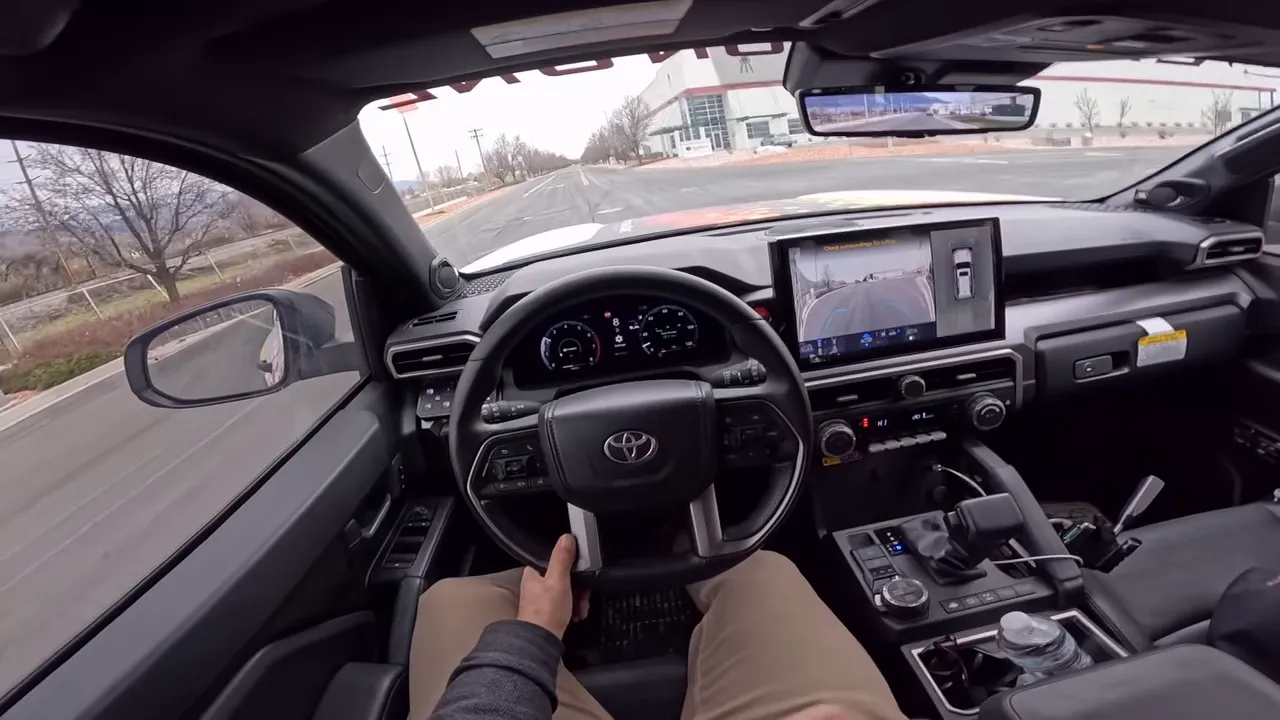 Driver POV inside Toyota 4Runner showing steering wheel, center touchscreen with camera feed and rearview mirror
