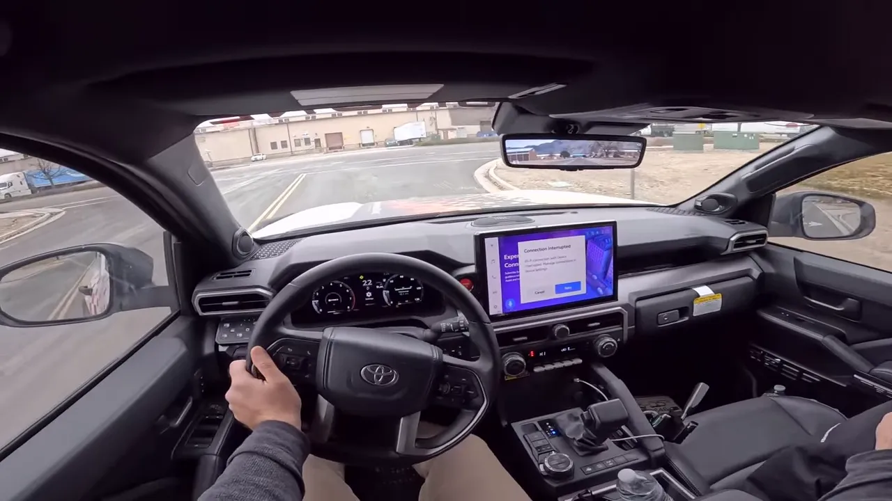 Driver POV showing steering wheel, center console with shifter and drive-mode/terrain controls and center touchscreen in a Toyota 4Runner