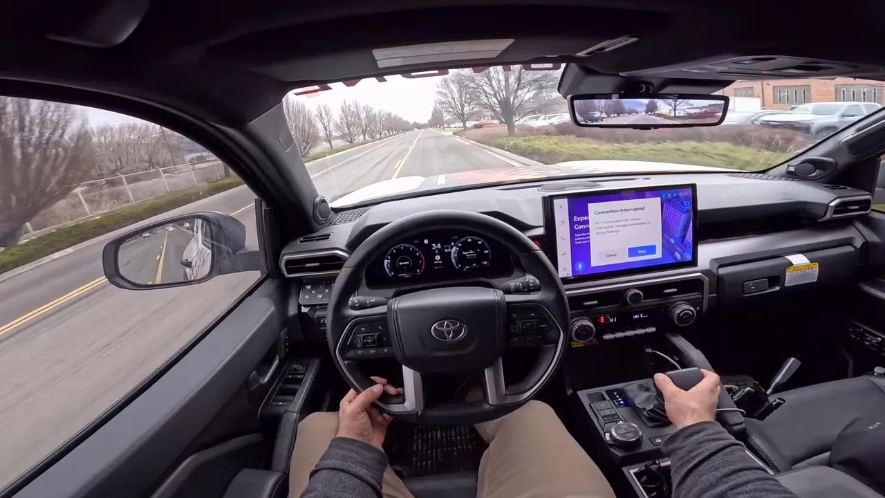 Centered driver point-of-view inside Toyota 4Runner showing steering wheel, readable instrument cluster, center touchscreen and road ahead