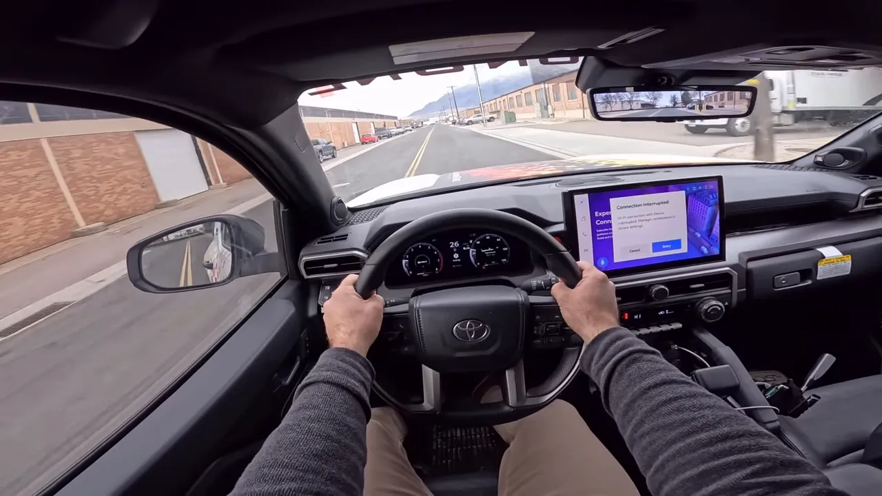 Driver POV inside Toyota 4Runner showing steering wheel, clear instrument cluster and center touchscreen with road ahead