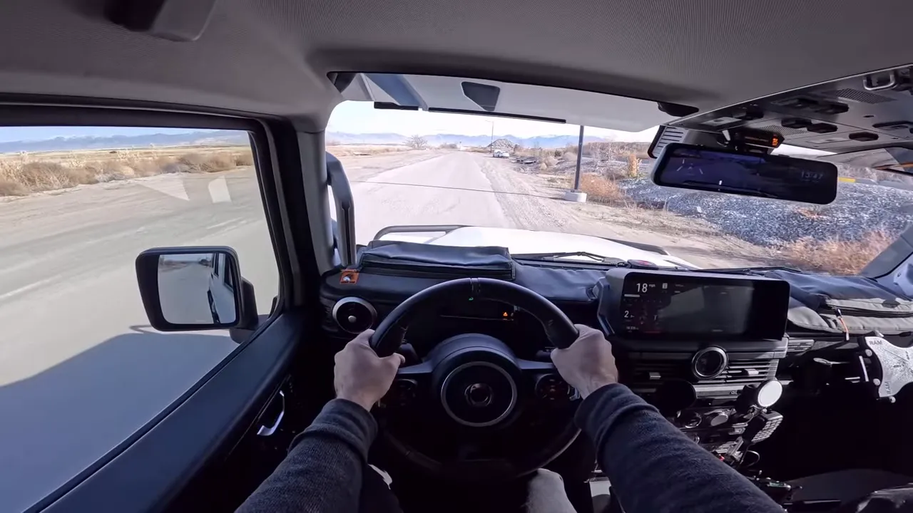Driver view inside Ineos Grenadier with hands on wheel, dashboard display and road ahead