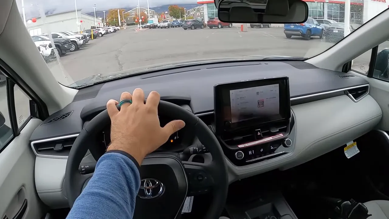 Driver view inside 2026 Toyota Corolla Cross showing a hand on the steering wheel, infotainment screen and the road ahead