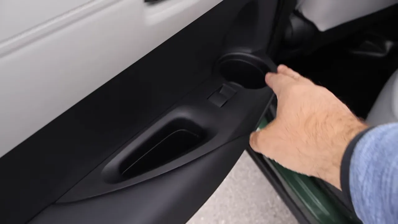 Interior rear door panel of the Corolla Cross showing an armrest and cup holder with a hand for scale.