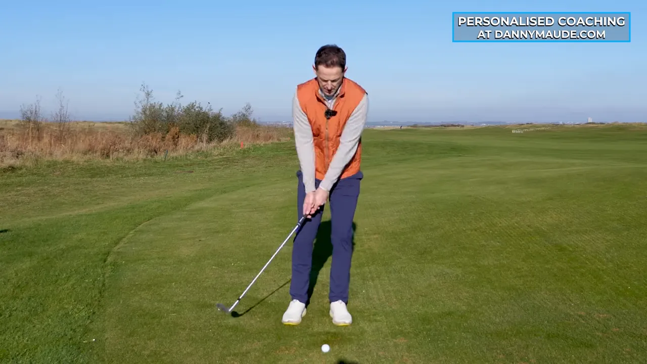 Golfer demonstrating an underarm-throw rhythm with a pendulum-like trail arm during a chip shot