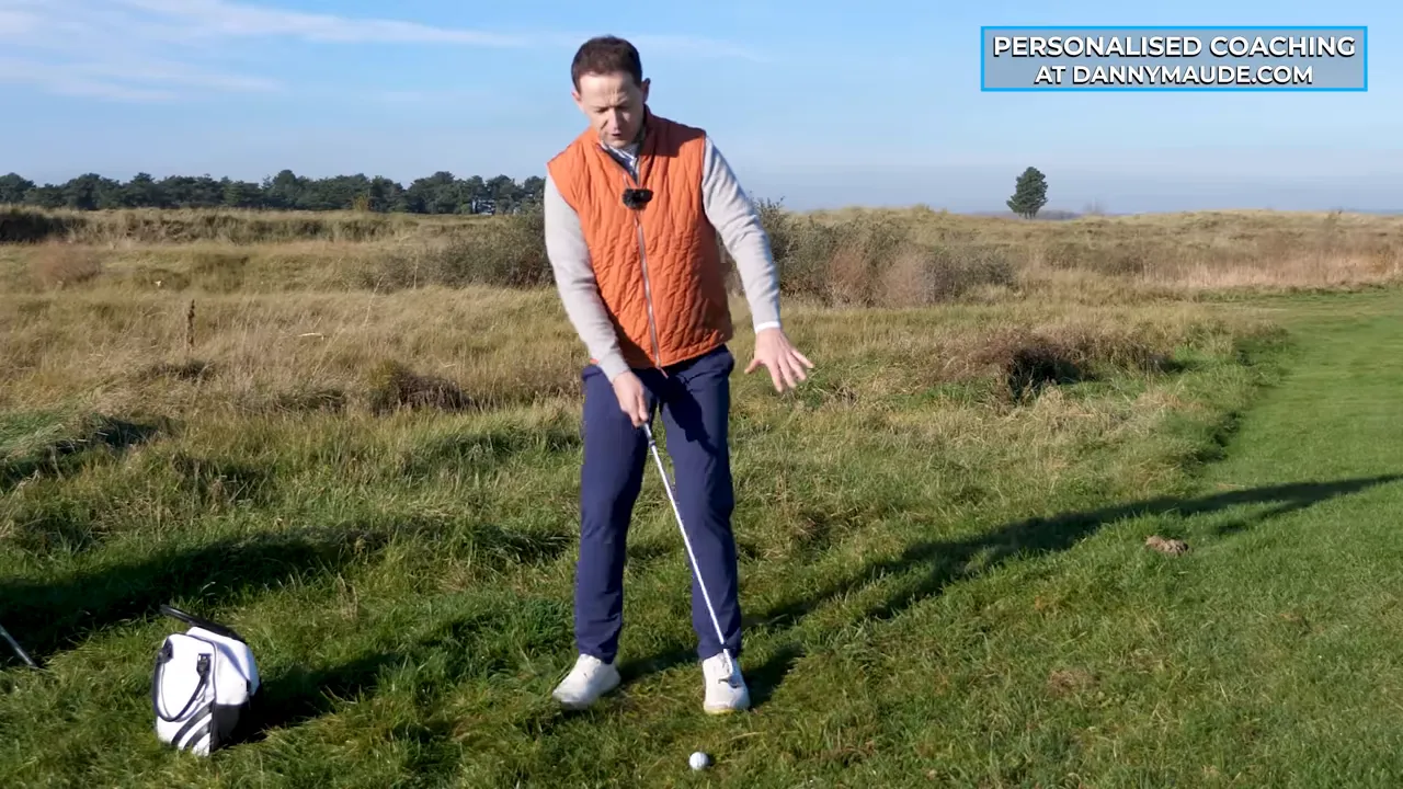 Golfer at address with hands on club, trail arm relaxed and palms-facing-forward, ball ahead of stance.