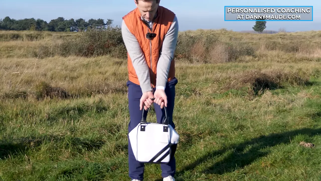 front view of golfer holding a white bag with both hands in front showing passive wrists and trail-arm position