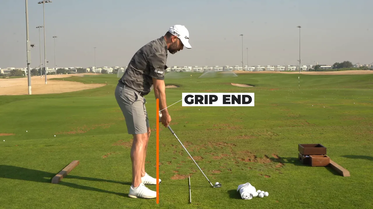 Golfer at setup showing grip end reference with vertical marker and hands between heels