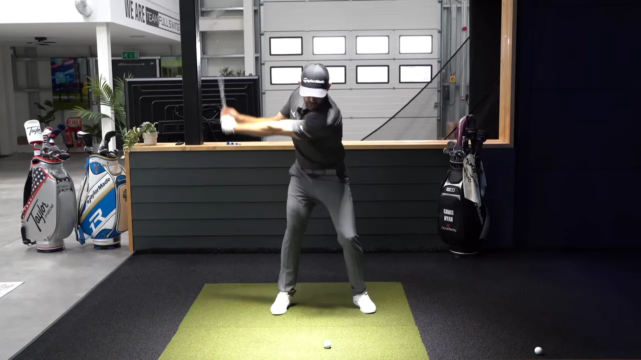 Golfer at the top of a half swing showing clear torso rotation and the chest/torch pointing toward the wall.