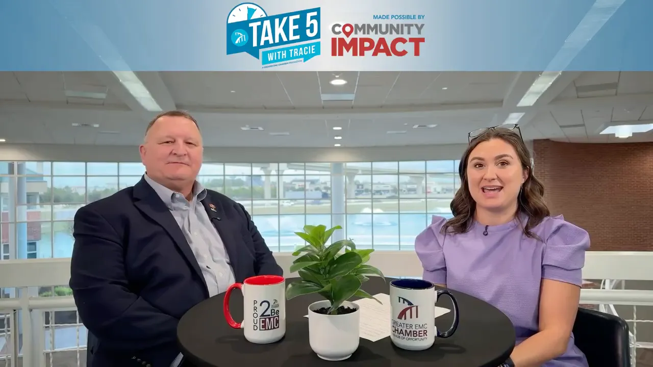 Two people seated at a small round table during an interview with show banner overhead