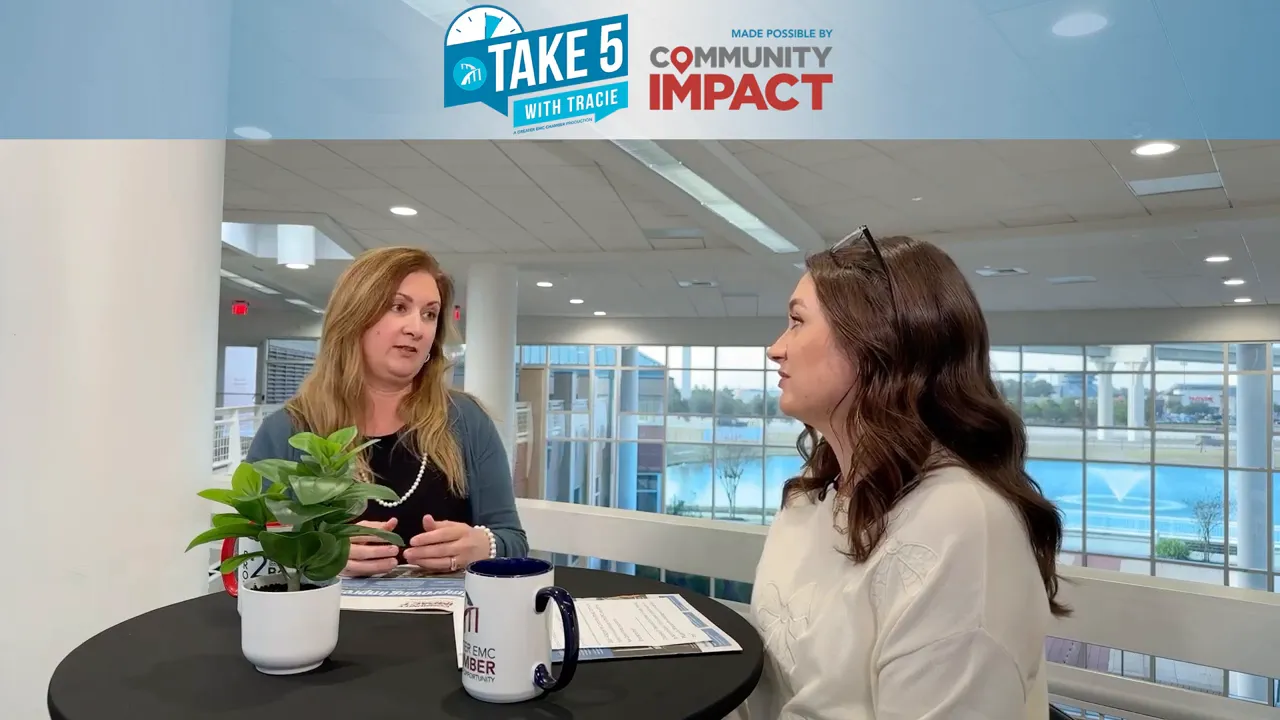 Wide shot of two presenters seated at a round table with printed materials and branded mug in an atrium setting