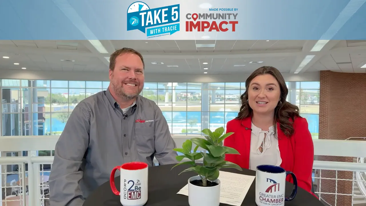 Interview shot of two people at a table with mugs and a small potted plant, in a bright public venue.