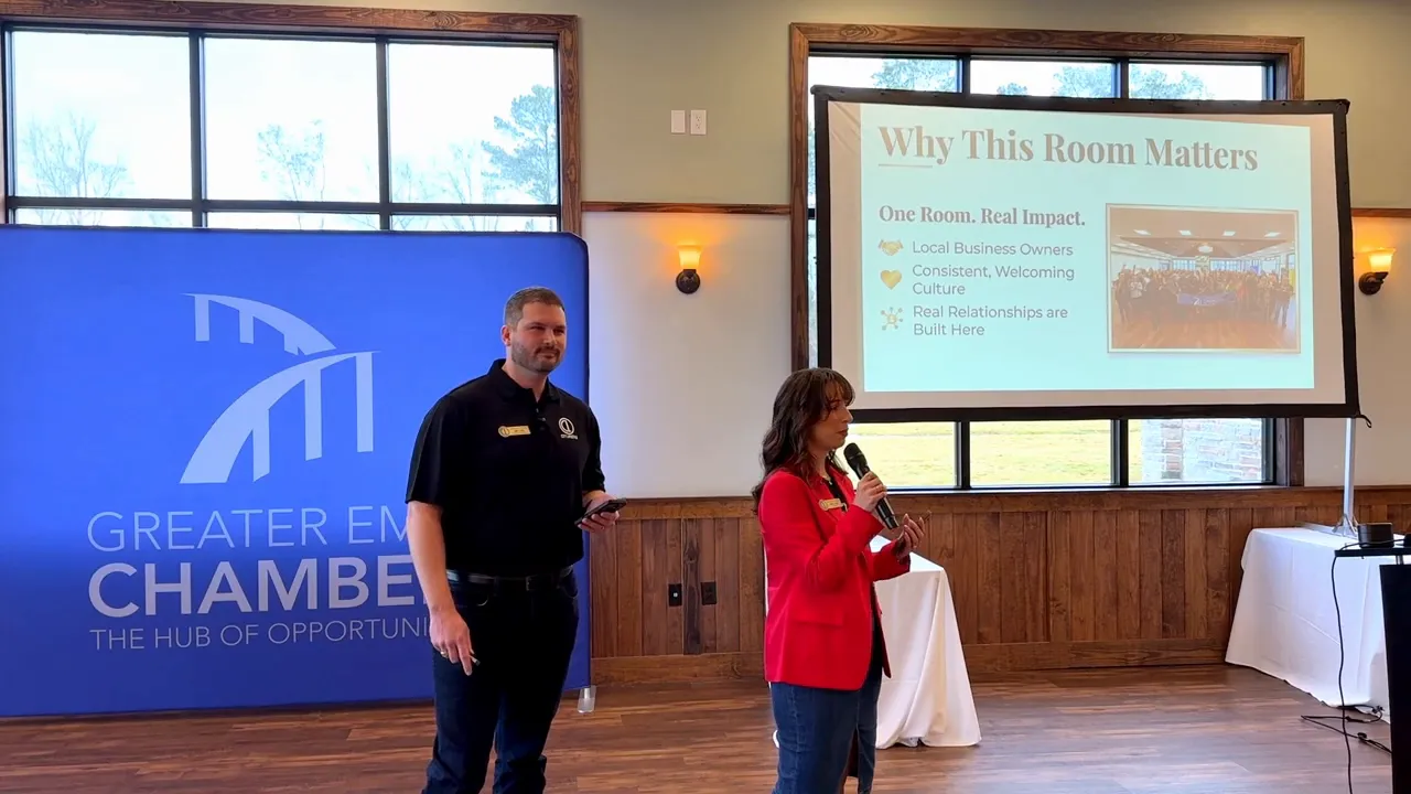 Two presenters on stage at the Business Networking Breakfast with a clear Greater Chamber banner and a slide titled 'Why This Room Matters'.
