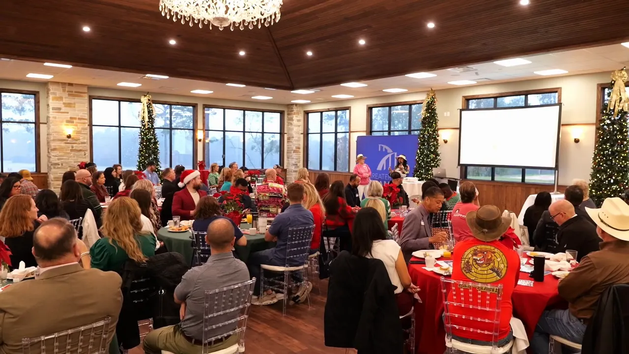 Wide shot of a networking breakfast event with tables of attendees facing a presentation screen and holiday decorations.
