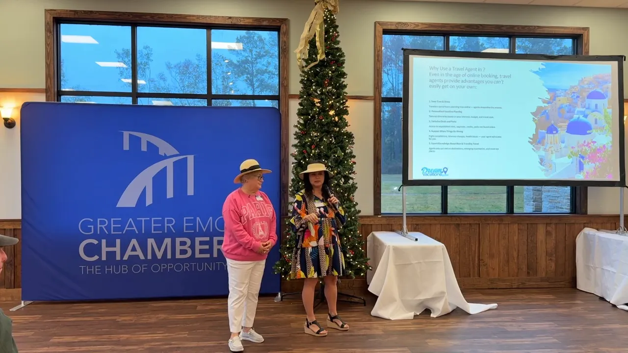 Two presenters standing by a projection screen and chamber backdrop during a business networking breakfast presentation.