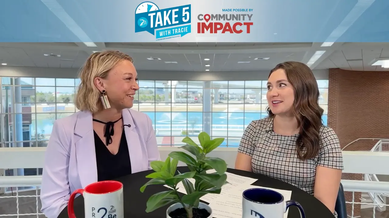 Two hosts smiling and engaged in an interview at a round table with a plant and mugs, 'Take 5' banner above.