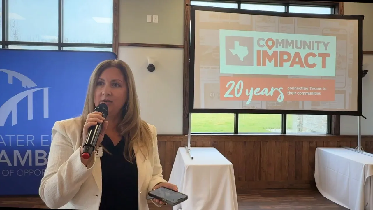 Presenter speaking into a microphone beside a projection screen that reads 'Community Impact 20 years'.