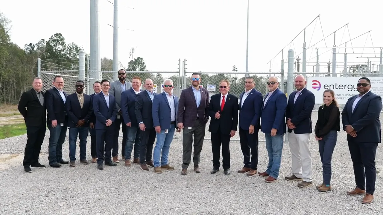 Group of Entergy and community representatives standing in front of a fenced substation with transformers and transmission equipment visible