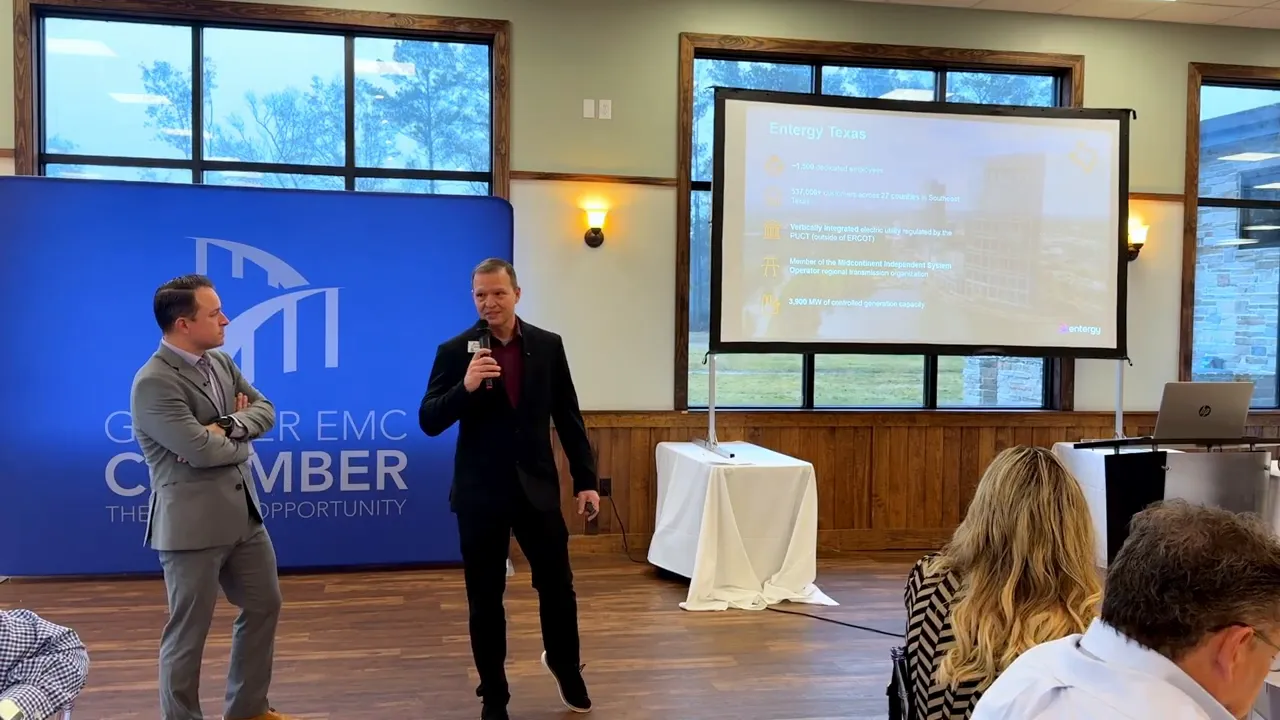 Presenter holding microphone beside a projection screen showing an 'Entergy Texas' slide at a business breakfast presentation.