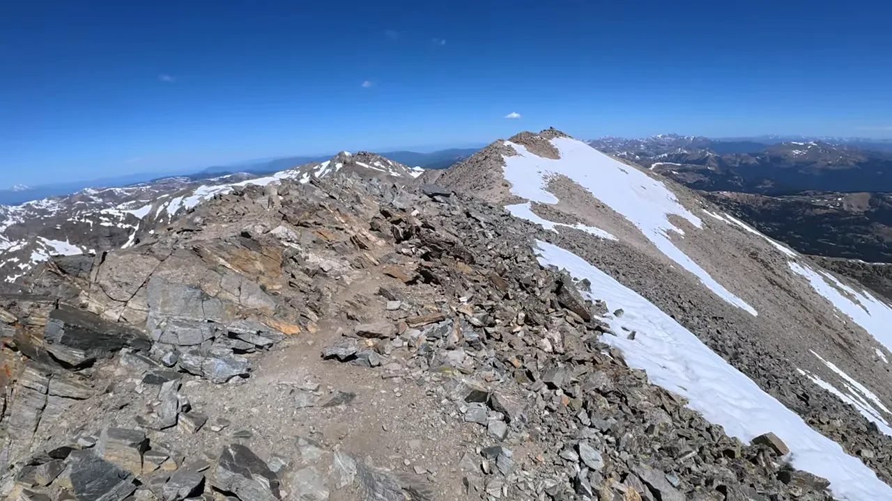 Rocky ridge extending toward a distant high point with snow along its right slope