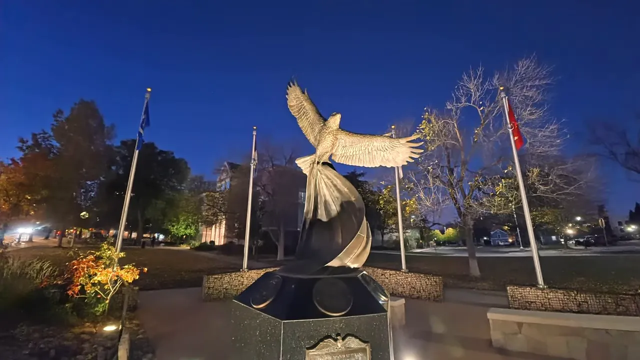 Night shot of an illuminated park statue and flags at dusk demonstrating low light image quality