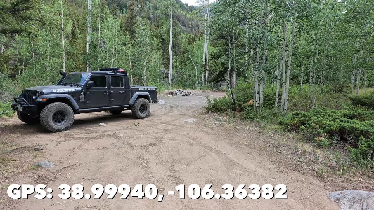 Pickup truck parked in a broad dirt campsite among aspens with GPS coordinates on screen