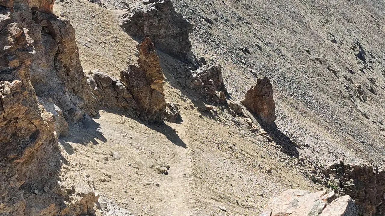 Loose dirt path beside rock towers with a steep rocky slope falling away to the right