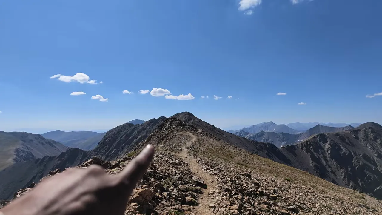 Narrow dirt path following a rocky mountain ridge toward a higher point
