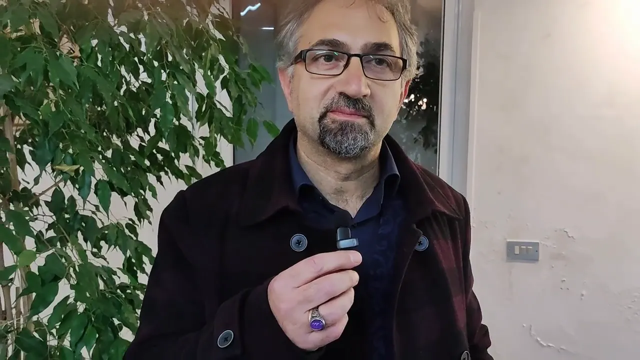 Relatore in piedi con microfono lavalier in mano, ripreso a mezzo busto in interno