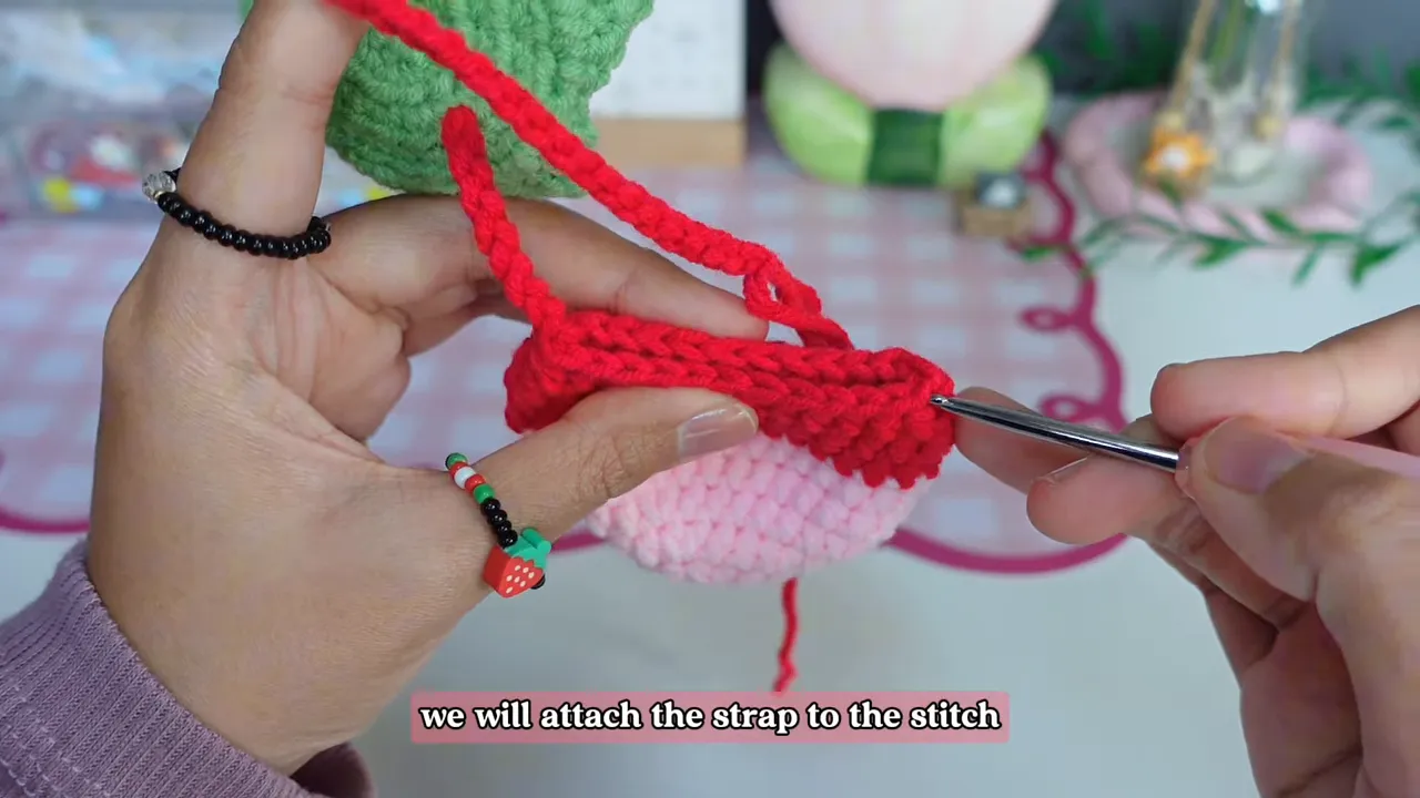 Crochet hook attaching the red chain strap to the top edge of the strawberry pouch