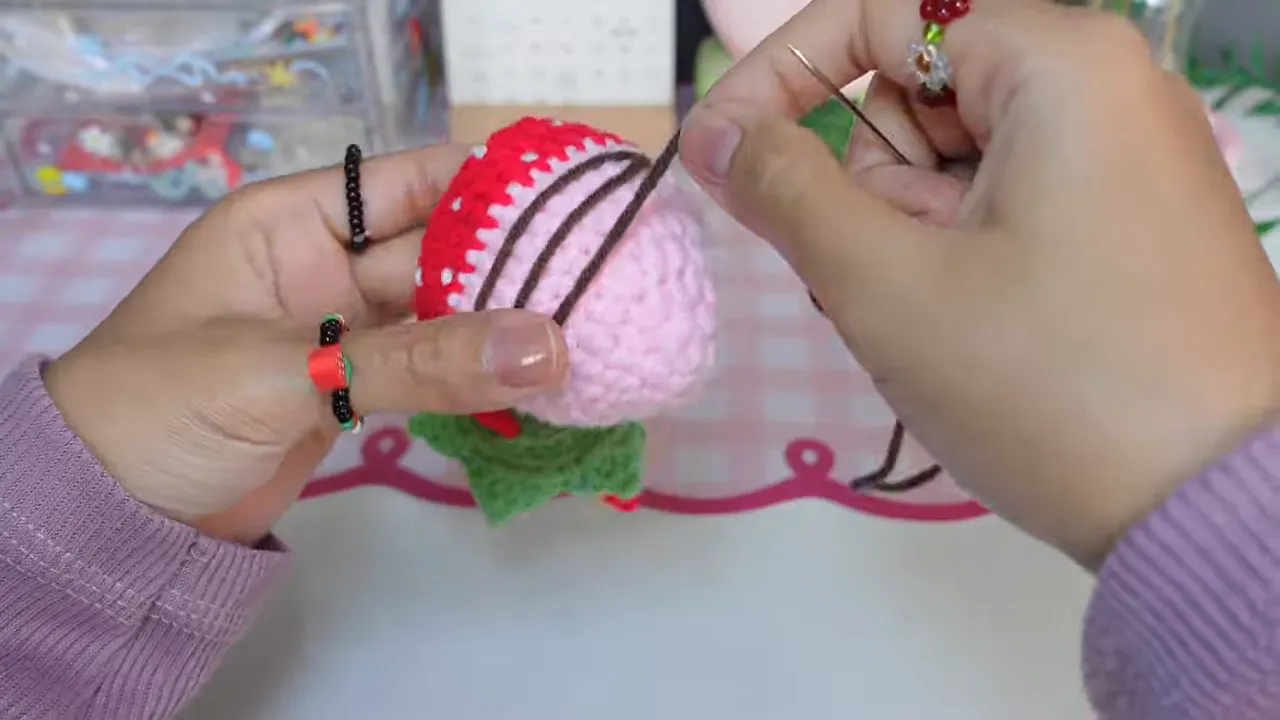Brown yarn embroidered in looping zigzag lines across the pink lower half of a strawberry pouch