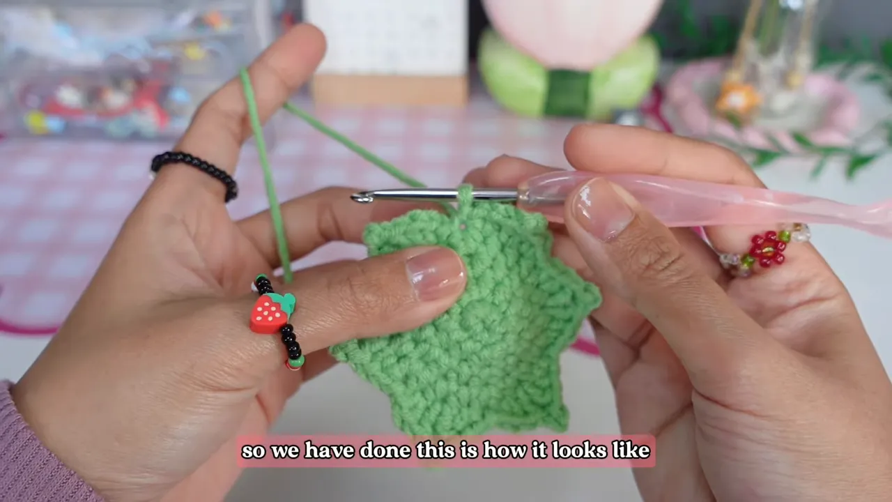Finished green crochet leaf cap with six pointed leaves held beneath a crochet hook