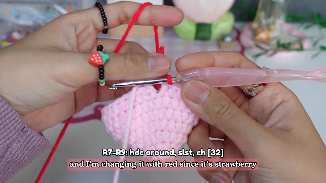 Red yarn being joined to the top edge of a light pink crochet pouch