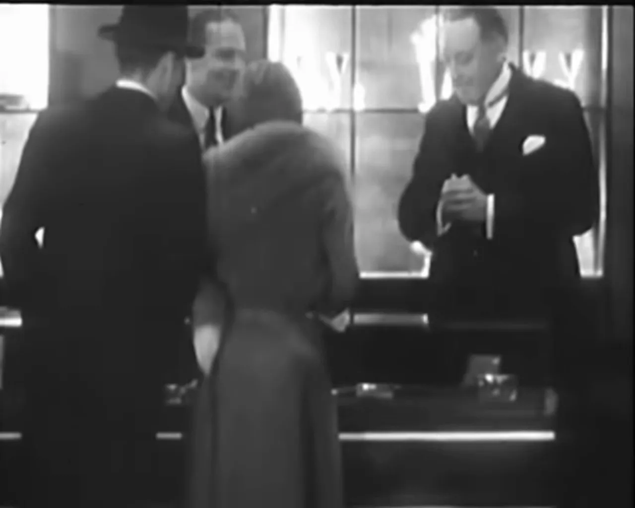 Customers at a jewelry counter talking with the shopkeeper over display cases in a close, well-lit shot.