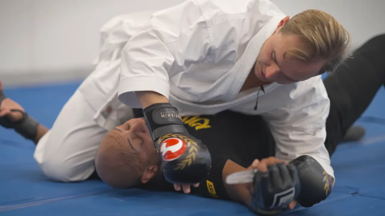 Top practitioner controlling the opponent's weapon-bearing arm on the ground in a topside crucifix-style position.