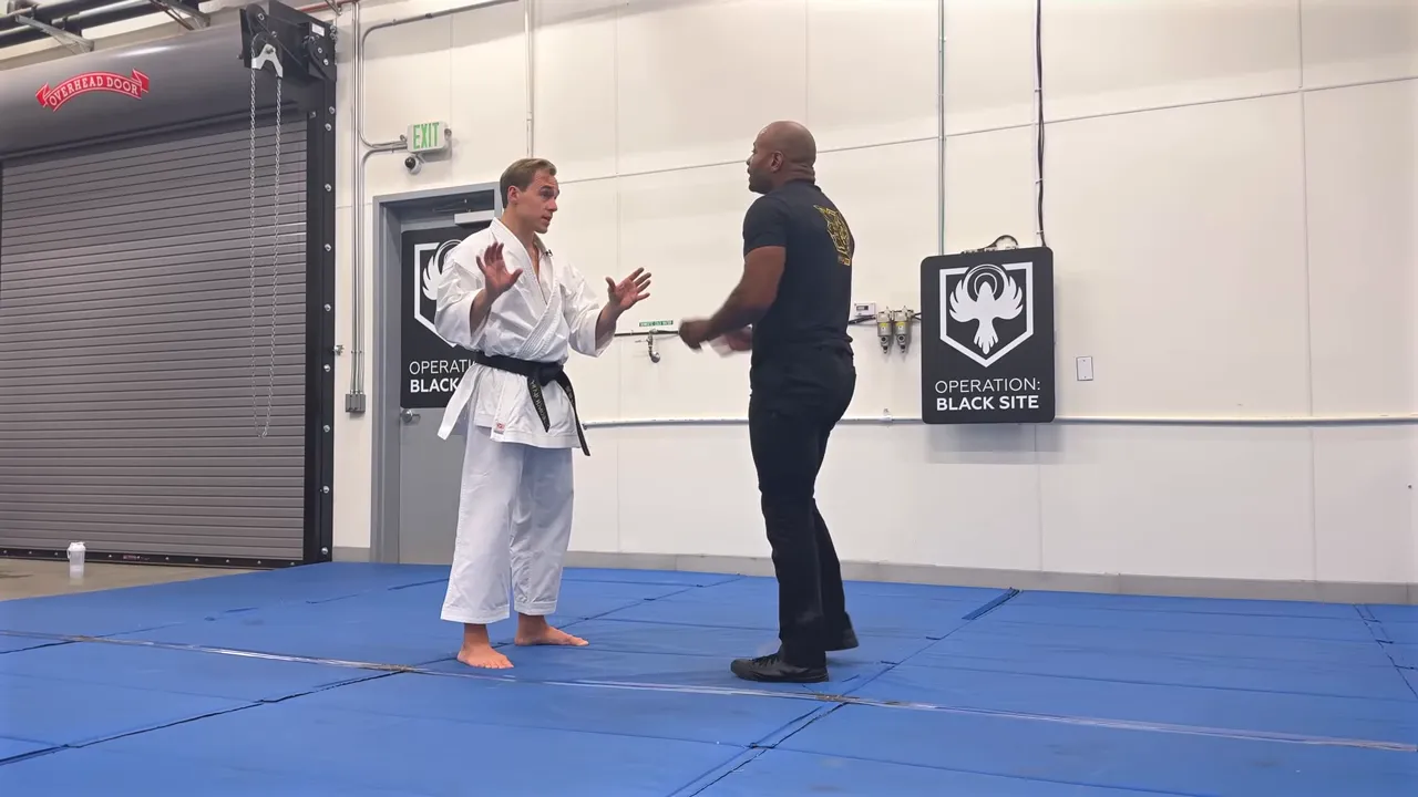 Karate practitioner and instructor facing each other on blue mats with hands raised, demonstrating conceptual training.