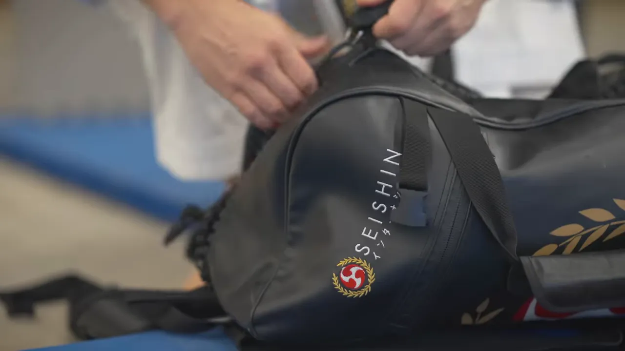 Close-up of a black training duffel bag being opened and adjusted on a mat