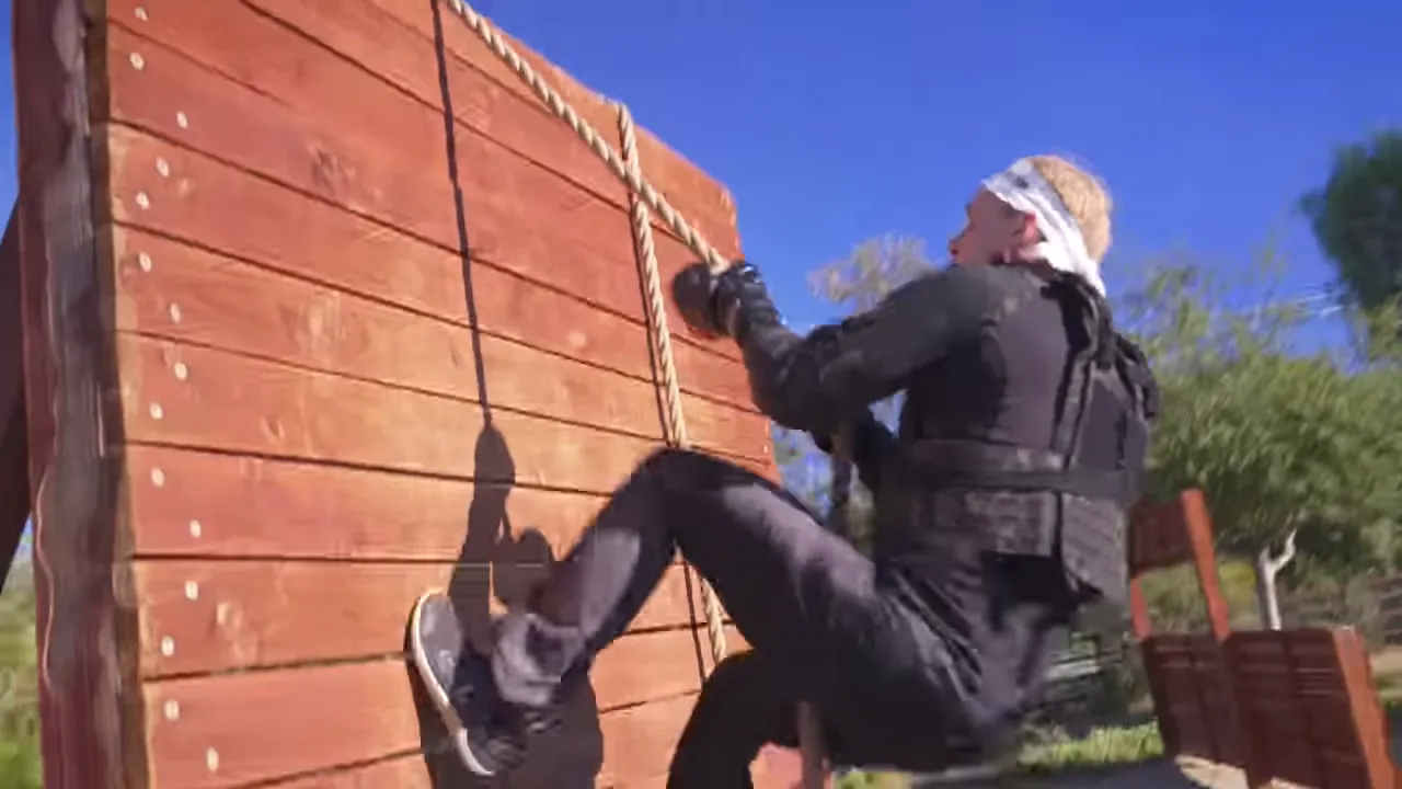 participant climbing a rope up a wooden wall wearing tactical vest and gloves