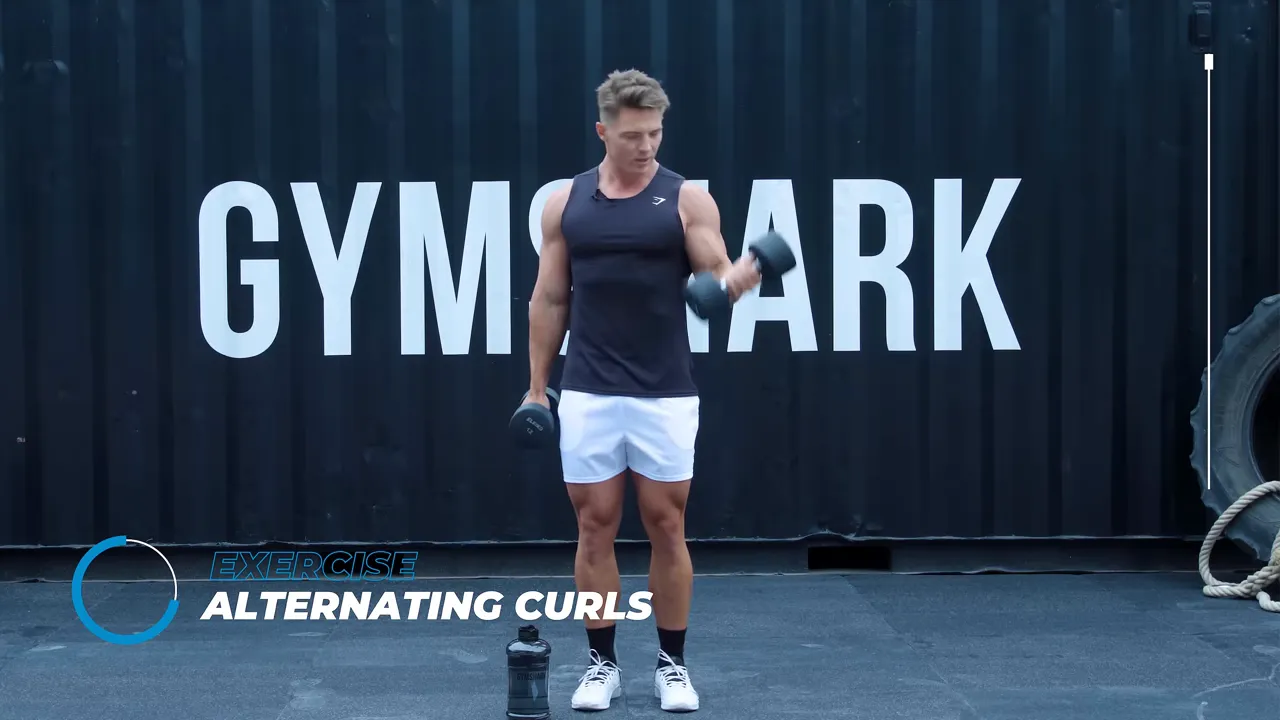 Full-frame shot of instructor performing an alternating dumbbell curl in front of a Gymshark backdrop