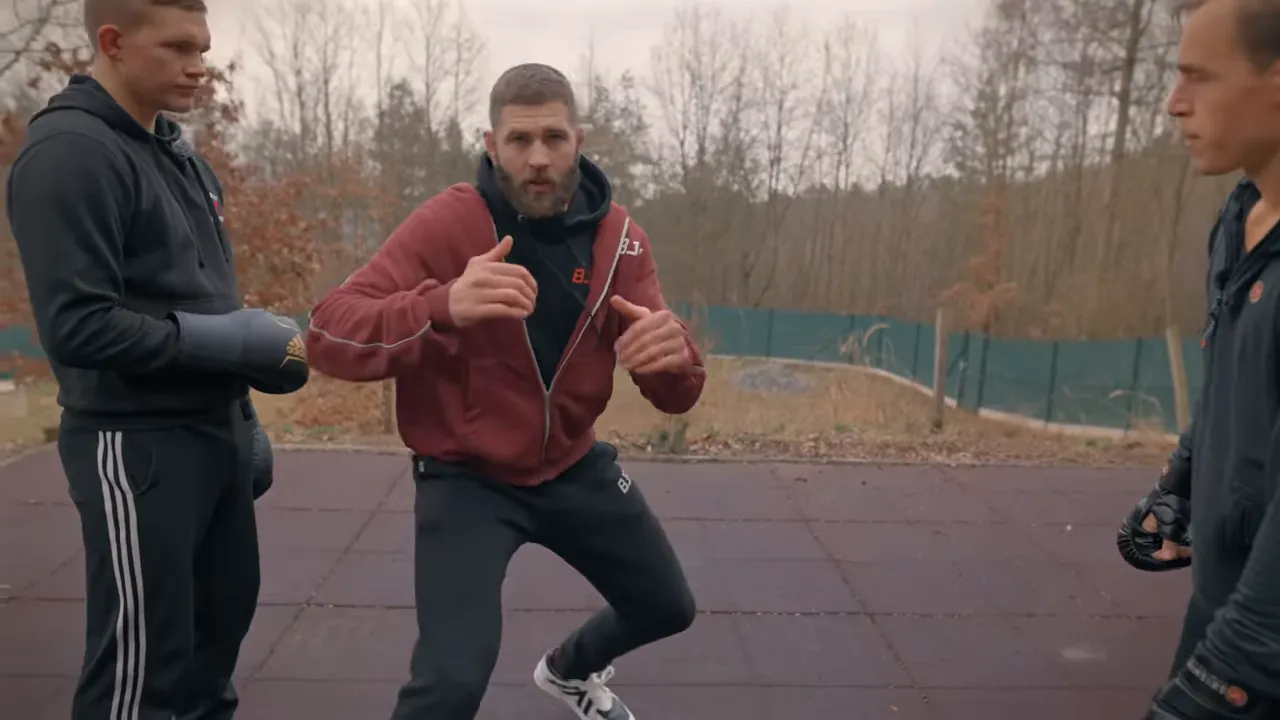 Coach demonstrating an angle step and forward pressure between two partners on outdoor mats.