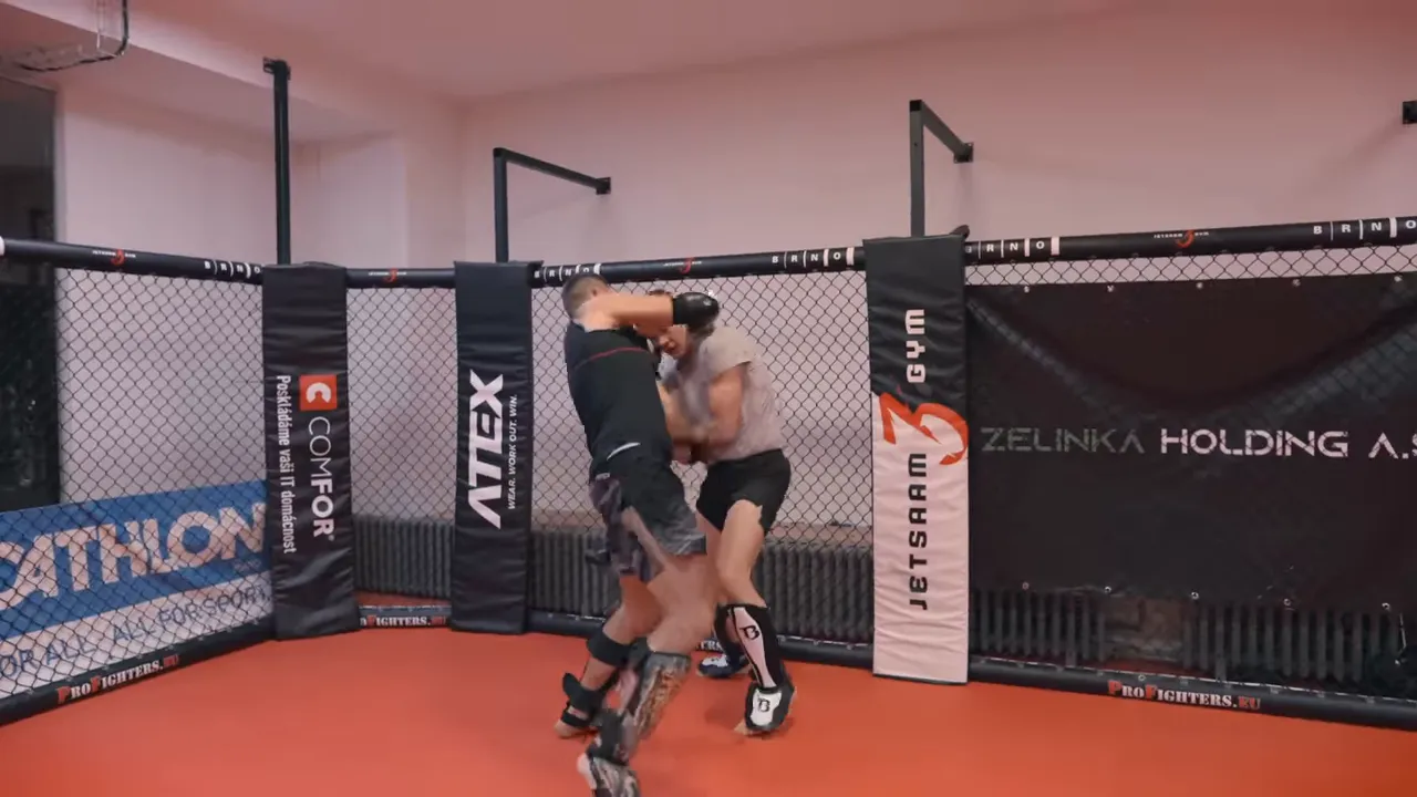 Two fighters in a controlled clinch against the cage during a sparring round showing pressure and footwork.