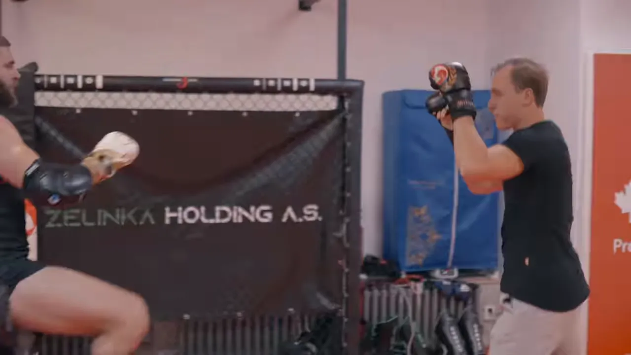 Two fighters in an MMA gym using a high forearm guard and distance to defend against a raised kick