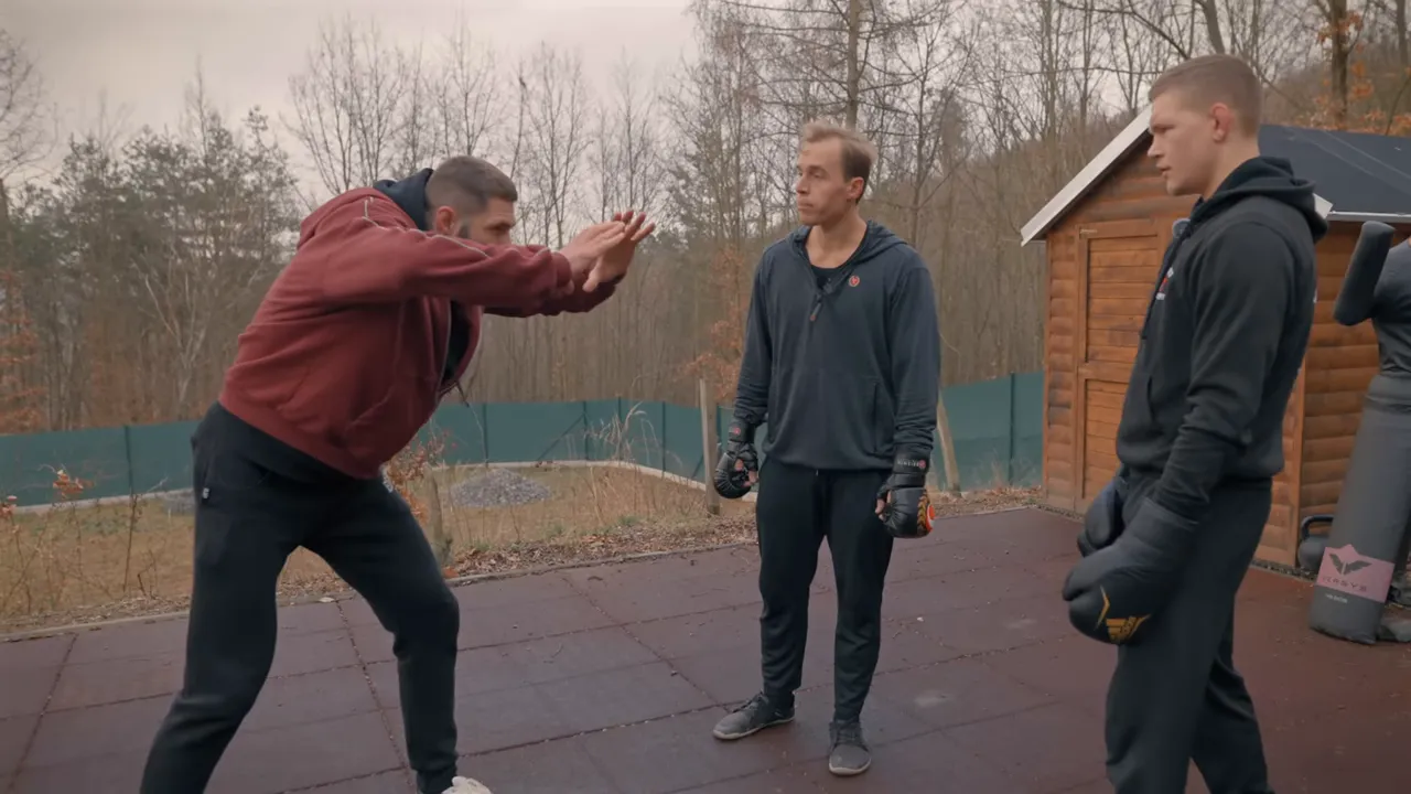 Coach leaning forward with hands extended demonstrating angle and distance while two students observe outdoors