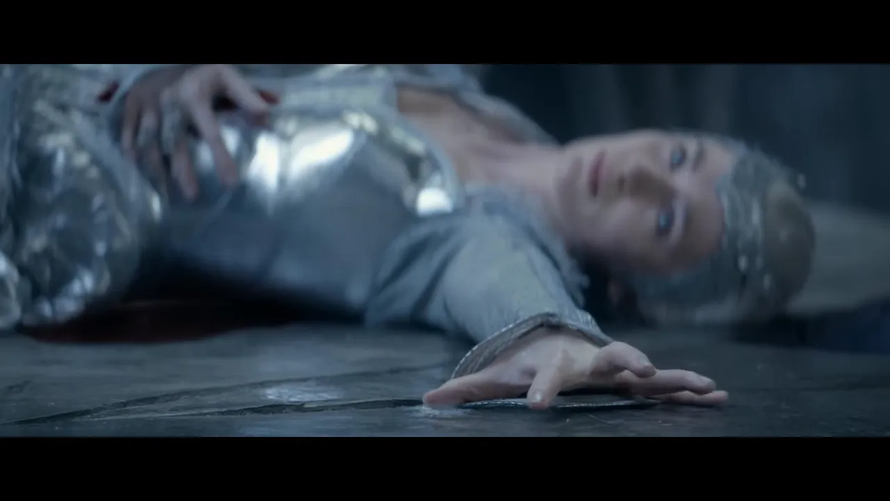 Woman in silver armour lying on a stone floor, reaching forward with an outstretched hand after a confrontation