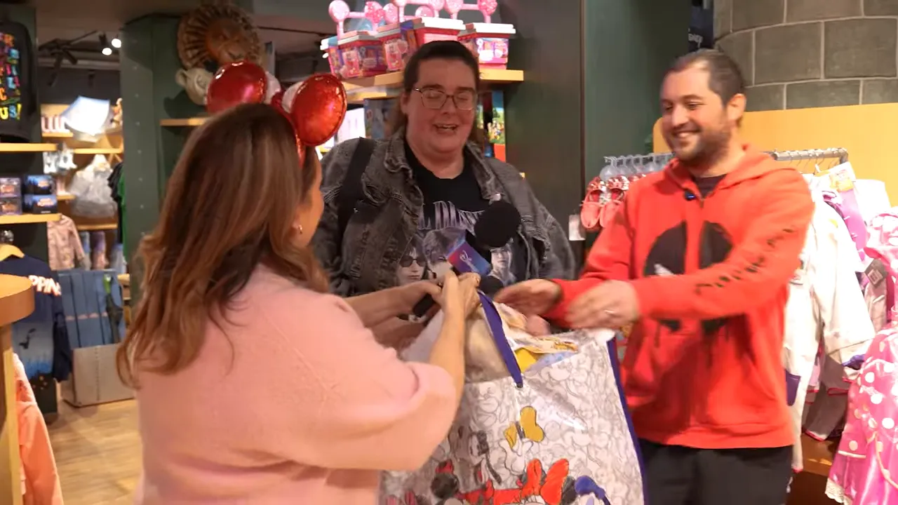 Presenter handing a large Disney tote to two smiling shoppers at a store checkout