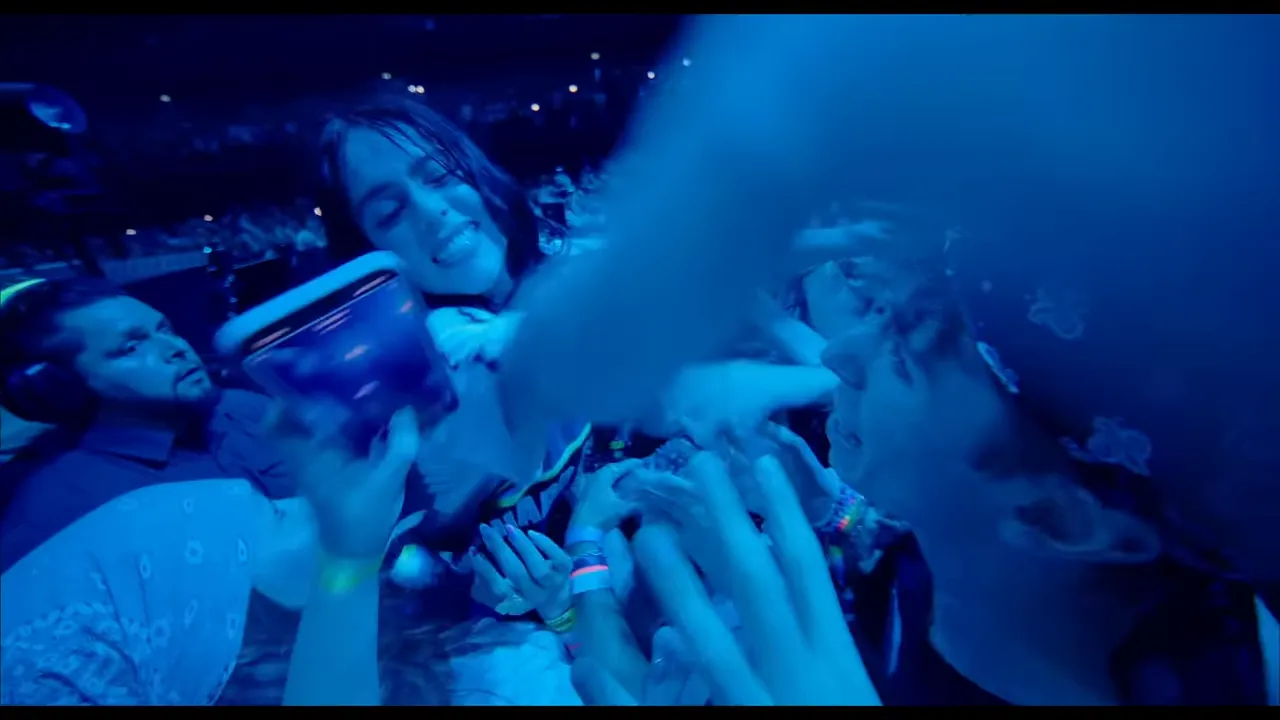 Performer leaning into the audience with multiple fans' hands reaching up under blue stage lighting.