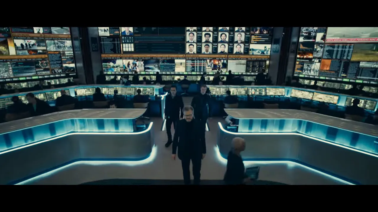 Wide control room with curved illuminated workstations and large wall of monitors showing multiple feeds